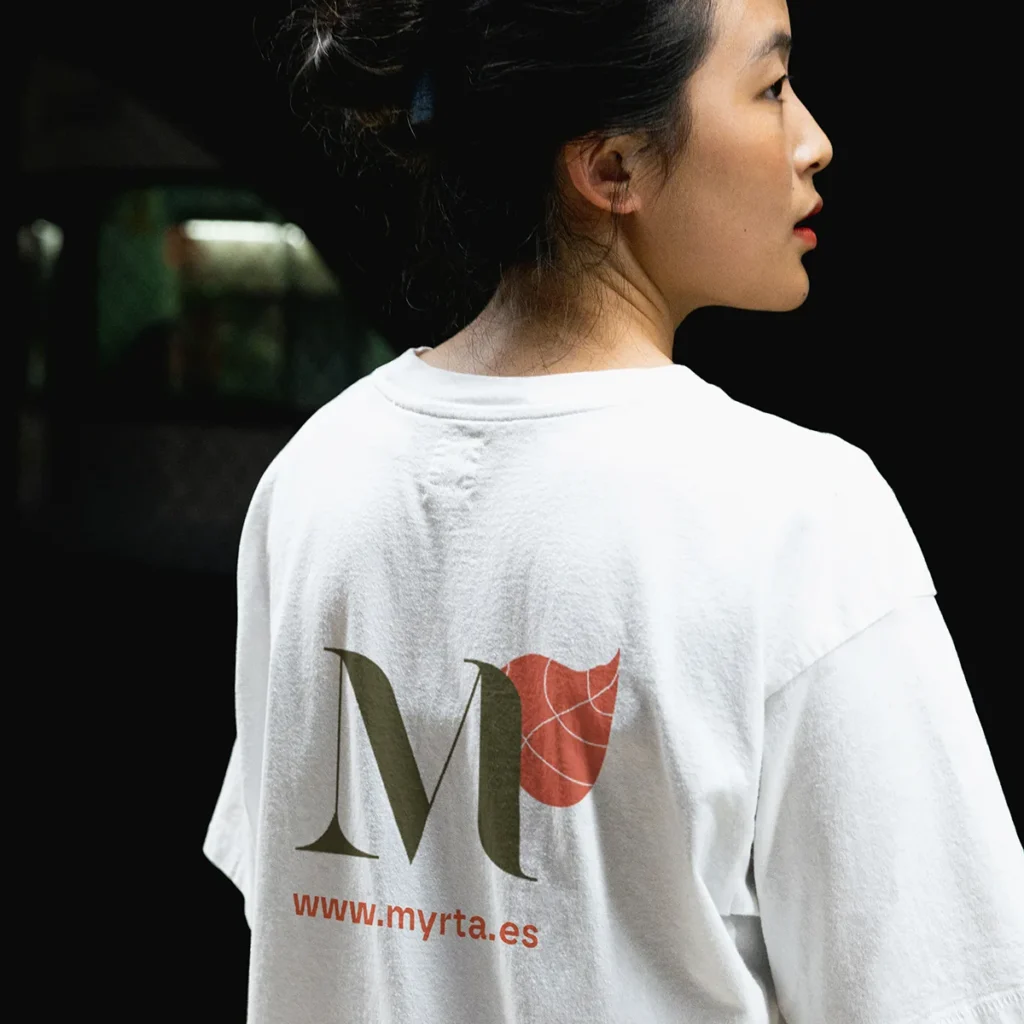 Chica vista de espalda con una camiseta con el símbolo de la marca Myrta que es una M verde y una hojita naranja en su parte derecha superior