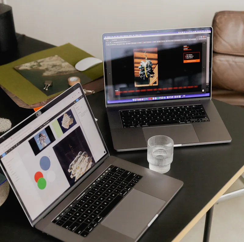 Dos portátiles sobre una mesa de madera negra y un vaso de cristal con agua